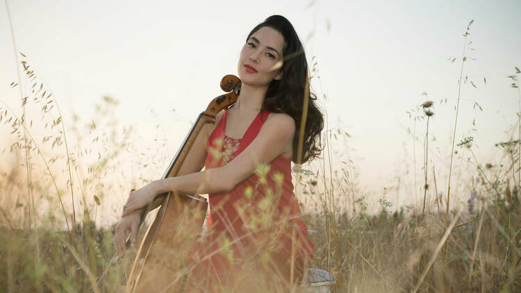 Cellist Kristina Reiko Cooper holds her cello in a field