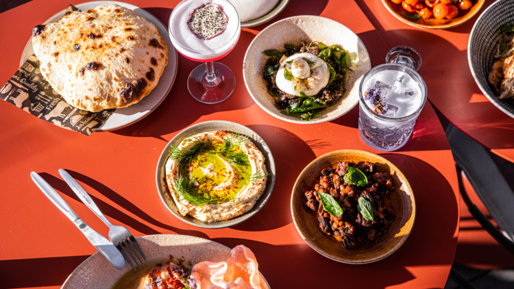 Food spread of woodfire puff bread, dips and burrata on a red table