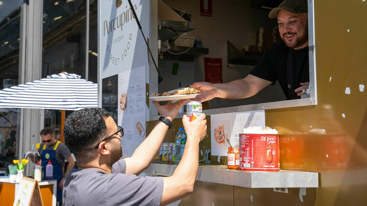 A person serving pizza out of a food truck.