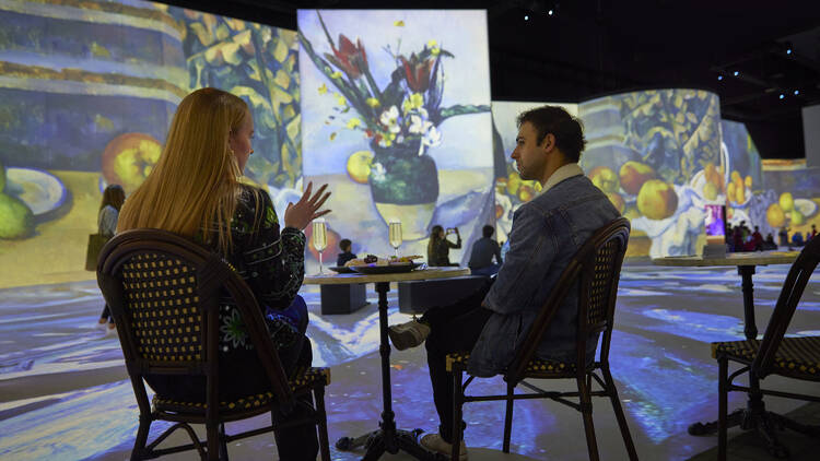 Man and woman sitting at a table inside an an illuminated, immersive art gallery. 