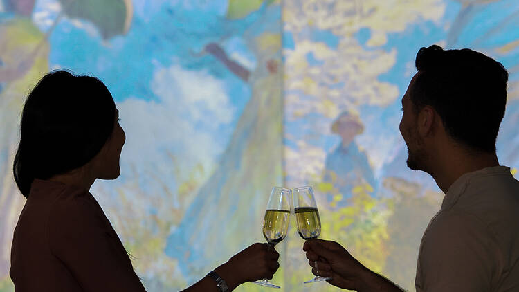 Man and woman toasting glasses of wine at a table in the foreground of a large digital art work.