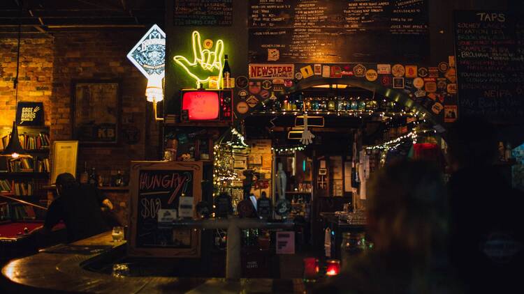 The interior of a dark bar with assorted neon signs.