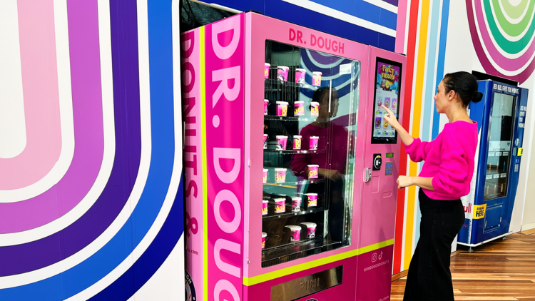 A woman touches a donut vending machine 