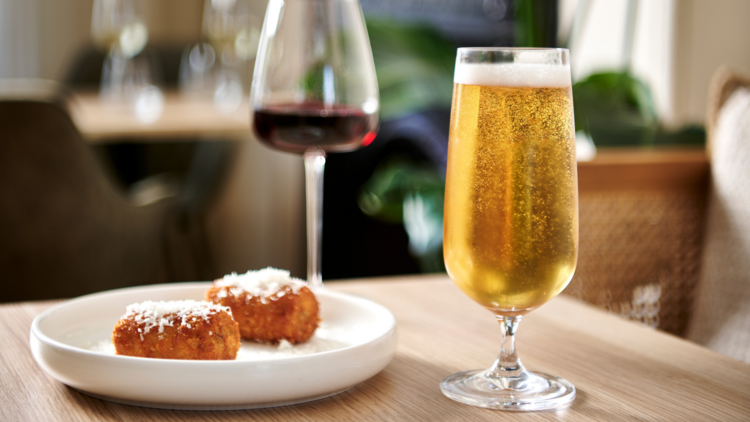 A beer glass with two arancini beside it