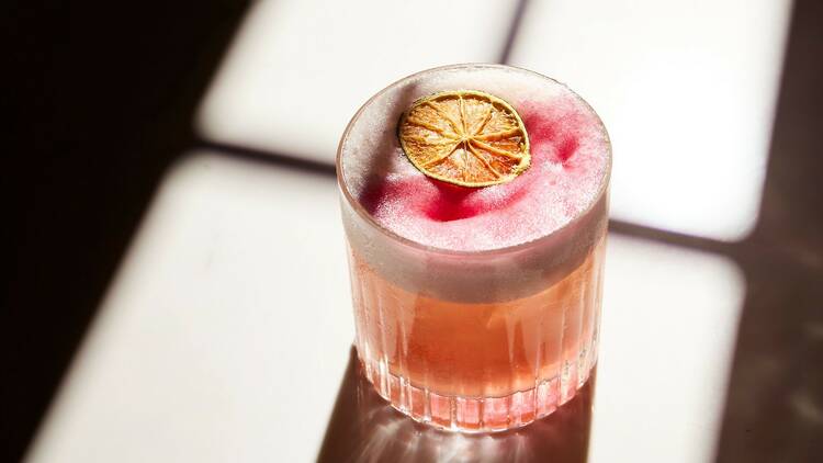 A gin and raspberry cocktail with a dried lime wheel on top.