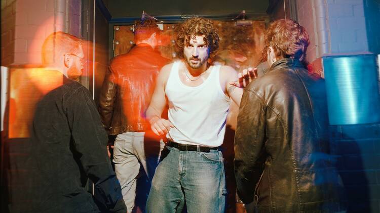 A man wearing jeans and a white singlet emerges from a club as others blur around him.