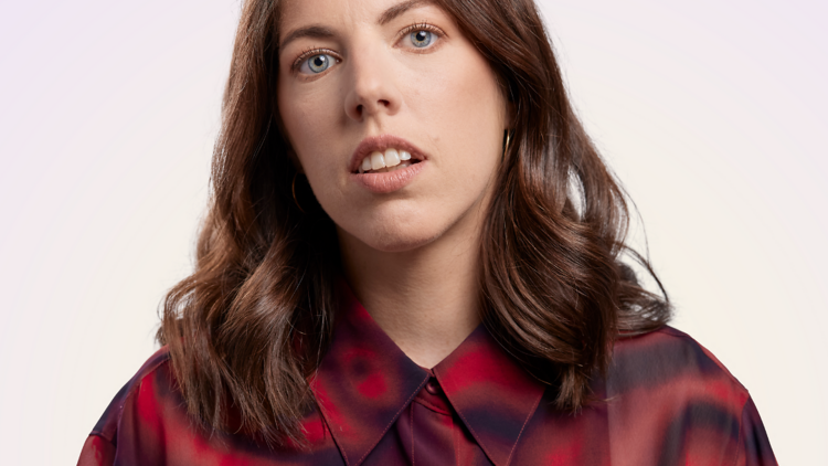 Comedian Alex Ward in a red shirt against a white backdrop.