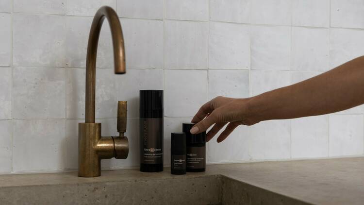 A hand reaches towards three elegant Synergie Skin products at a fancy sink.