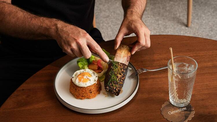 Man slicing meat off a beef short rib onto a plate of kimchi fried rice topped with an egg and salad.