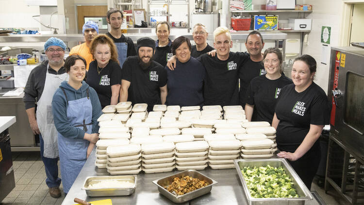 A group of chefs and volunteers stand together in a kitchen.
