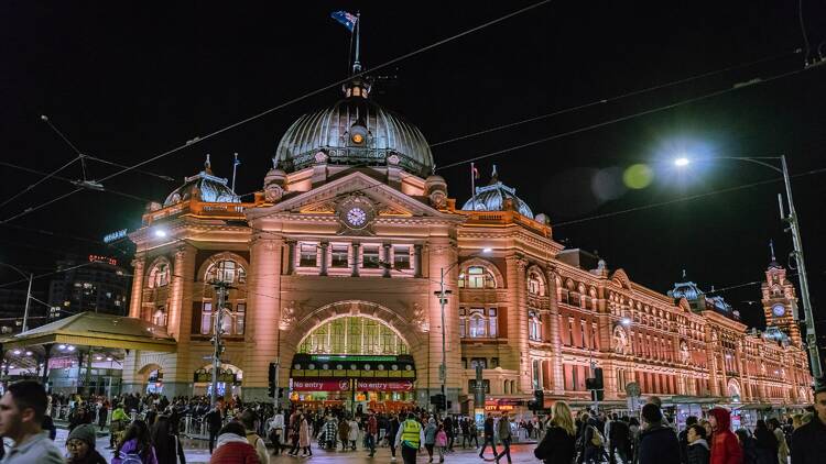 Flinders Street Station in Melbourne at night with crowds of people.