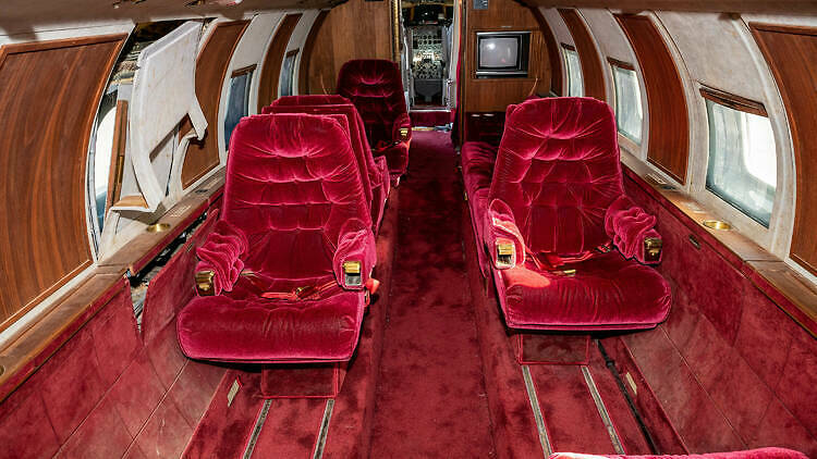 "Interior shot of Elvis's jet shows red velvet seats on either side of the red carpeted aisle, in poor shape.