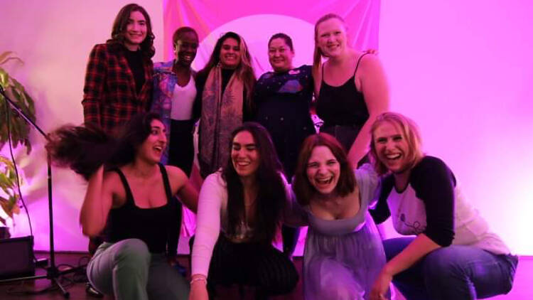 A group of comedians in front of a pink background.