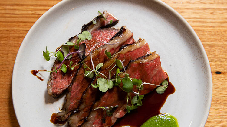 Sliced meat plated with a verdant green sauce on a wooden table.