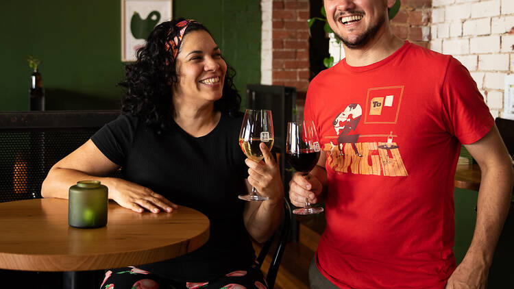 Keyma Vasquez and Sergio Tourn smiling with a glass of wine each at a wooden table.