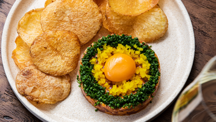 Beef tartare with an unbroken egg yolk on top, surrounded by potato crisps.