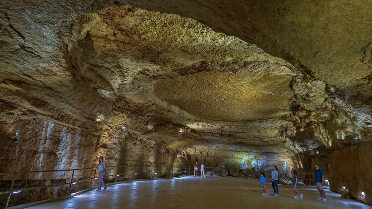 A vast underground cave space with a few people on the ground looking up at the dome.