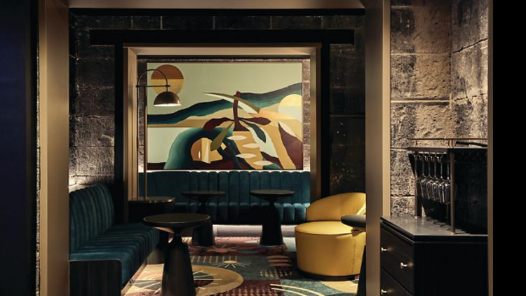 Large modern piece of art work in a wine bar with plush green sofas, colourful rugs and bright yellow ottomans.