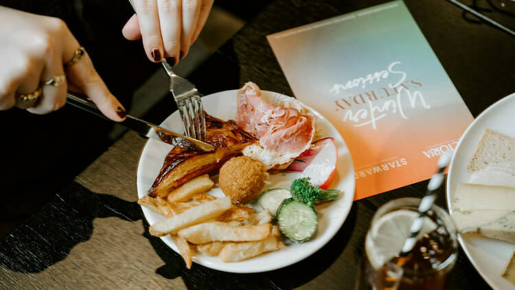 A diner digging into a plate of assorted lunch items placed next to a menu.