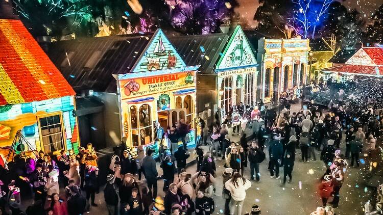 A crowd passes in front of illuminated shopfronts at Sovereign Hill.