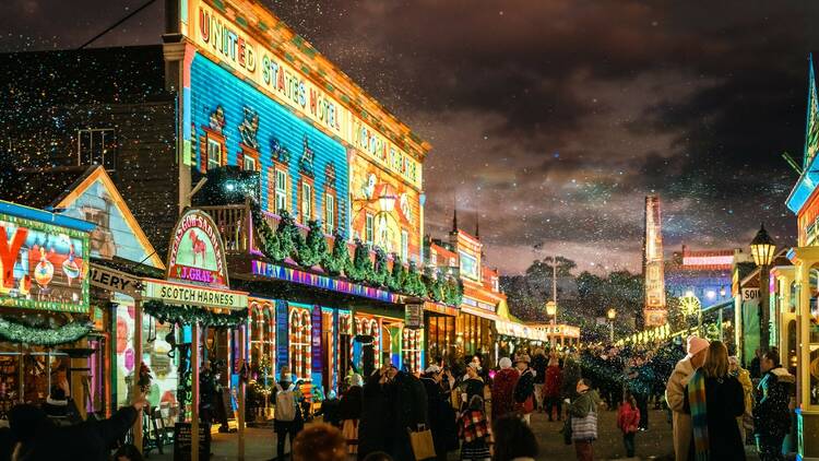 A crowd passes in front of illuminated shopfronts at Sovereign Hill.