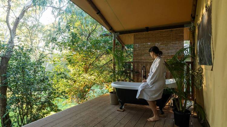 A woman about to take a bath on an outdoor deck overlooking bushland