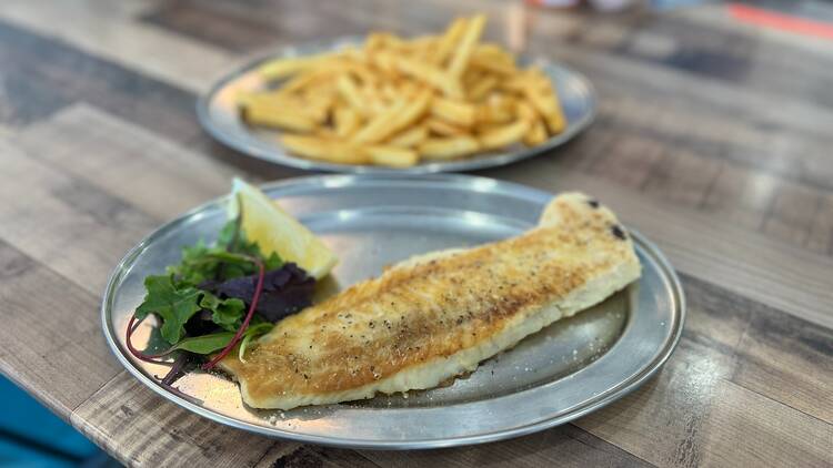 A grilled piece of cod, salad and chips