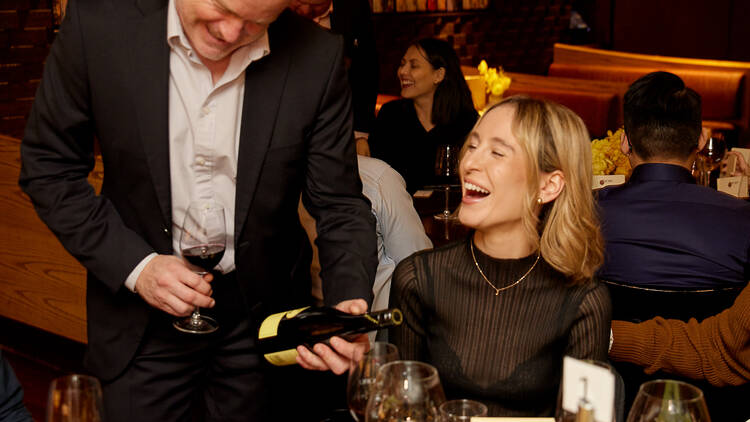 Ben from Petaluma wines pouring wine for a laughing blonde woman inside the Nobu restaurant.