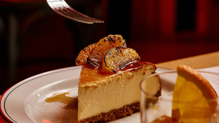 Fork poised over a ricotta cheesecake next to a cocktail. 