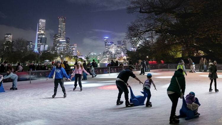 People skate on an ice rink with the city skyline in the background.