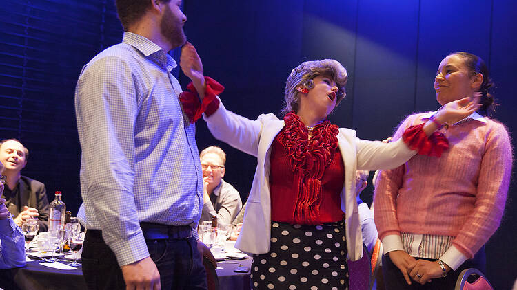 An actress dressed like Sybil Fawlty is talking to two people who look baffled.