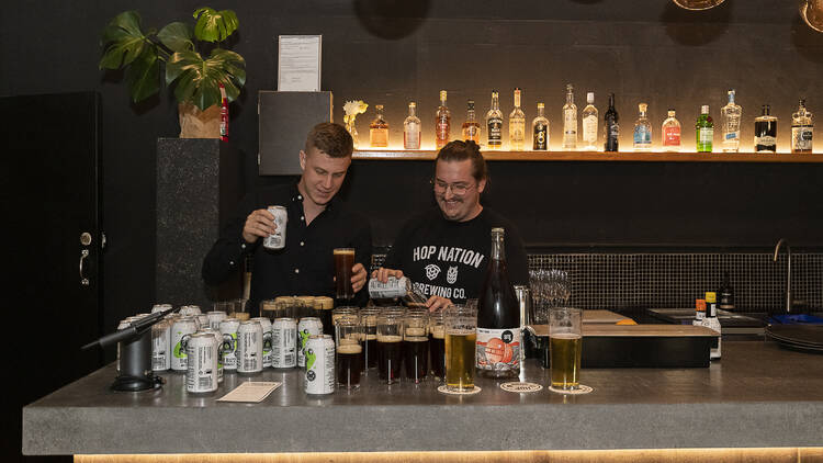 A pair of brewers pouring pints of beer behind a backlit bar.