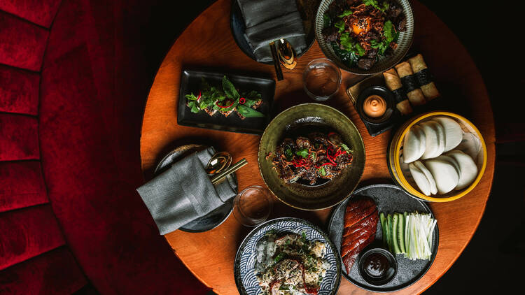 Asian food on a table, with a red velvet lounge.