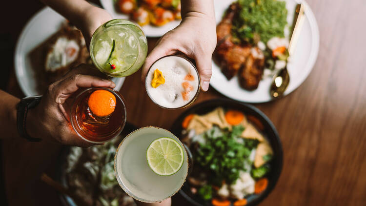 People cheersing cocktails above a table full with food.