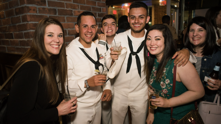 Three sailors in uniform pose for a photo with a group of women.