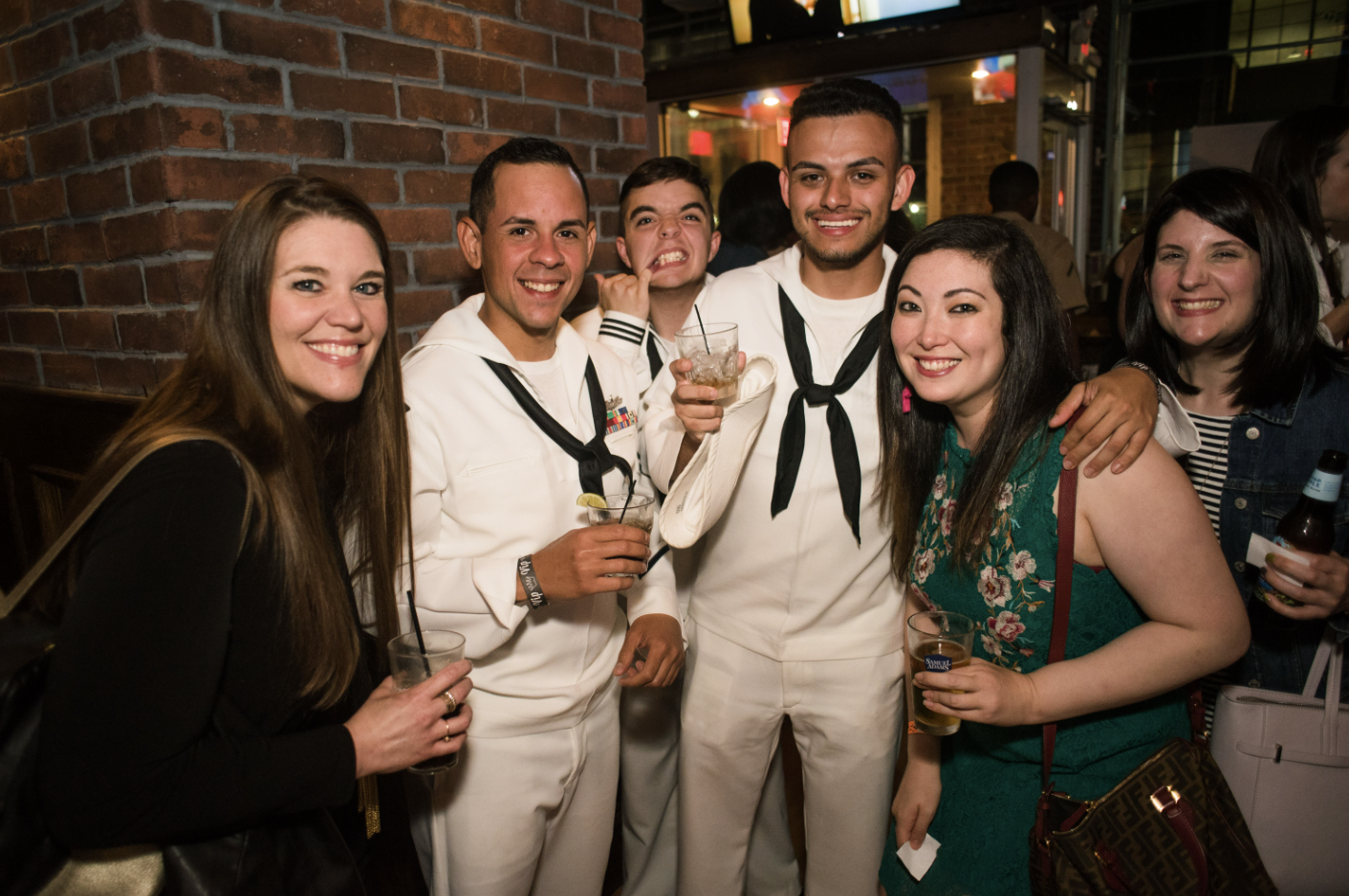 Three sailors in uniform pose for a photo with a group of women.