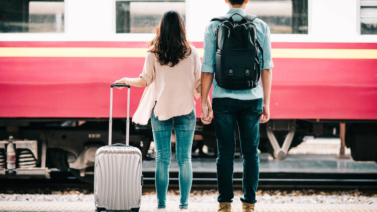 Back view of loving couple tourist holding hand at train station.