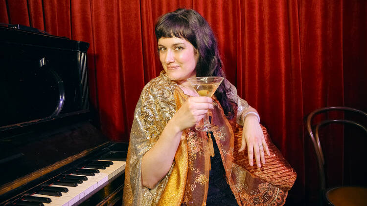 A performer sits at a piano holding a martini.