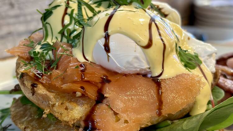 A breakfast stack including poached eggs, smoked salmon, a creamy sauce and fresh green herbs.