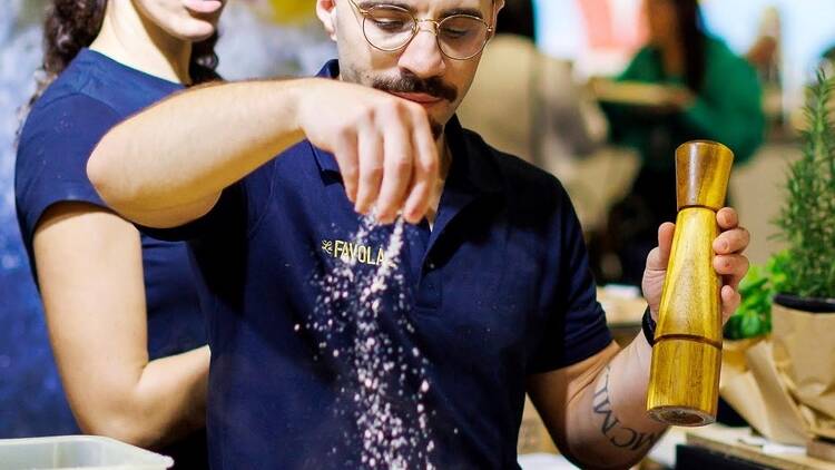 Man sprinkling salt into a parmesan wheel of pasta.