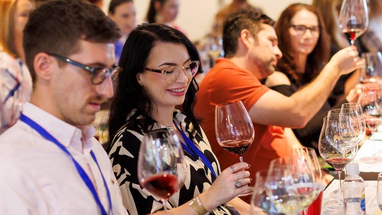 Show attendees swilling and tasting wine at a table. 