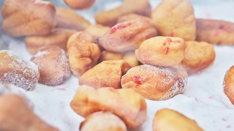 Hot jam doughnuts in a bowl of icing sugar.