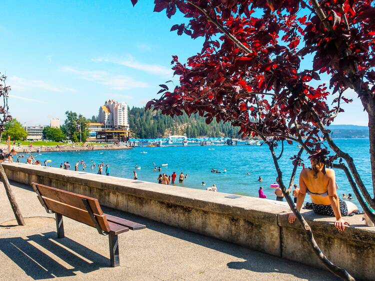 A woman relaxes on a barrier wall at the City Beach and Park along the shores of Lake Coeur d'alene, Idaho on a busy summer day.