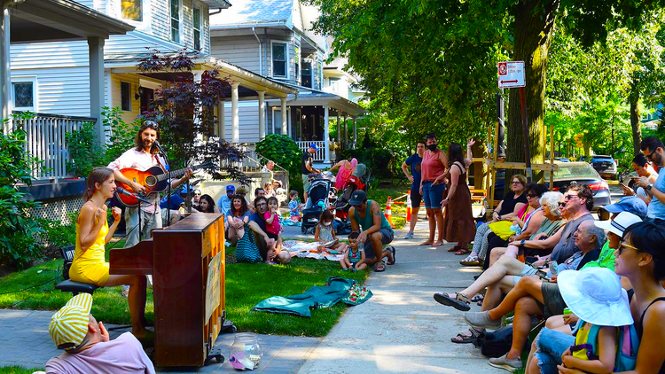 A group of musicians on a front yard playing for a crowd sitting on the grass.
