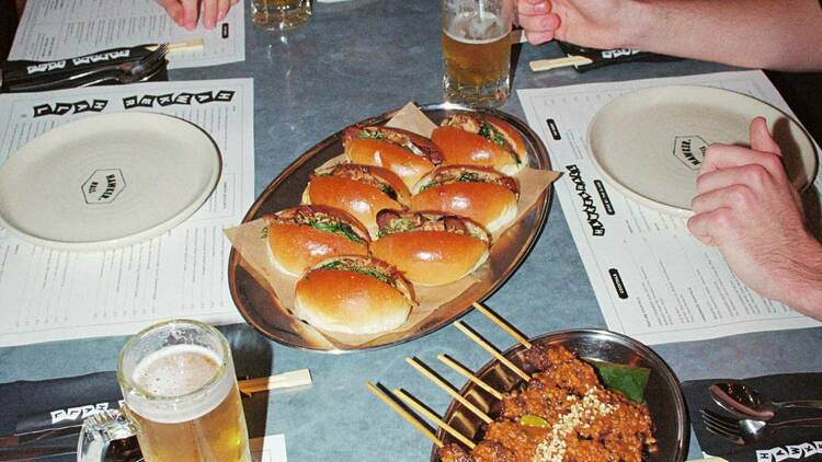 People sitting at the table around beers and plates of food. 