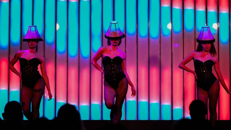 Three women dance on stage with lampshades on their heads.