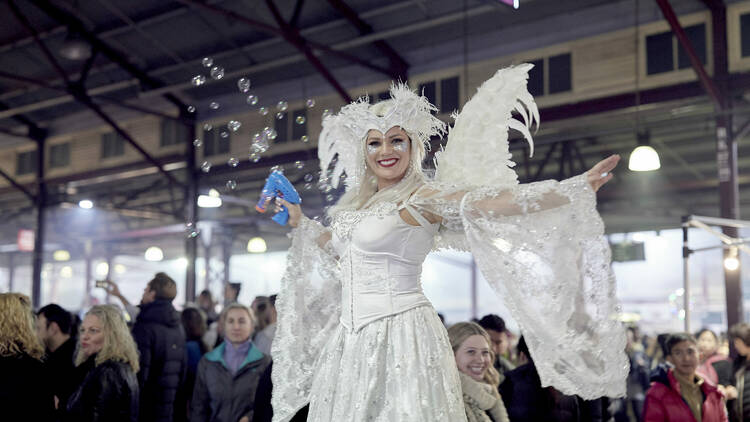 A person dressed in a white fairy outfit at a night market.