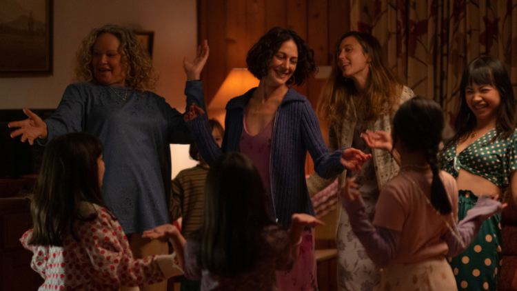 A woman dancing with lots of young girls and women in a living room