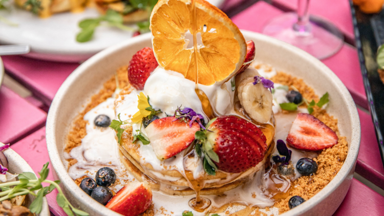 A plate of pancakes puled with fruit, ice-cream and syrup.