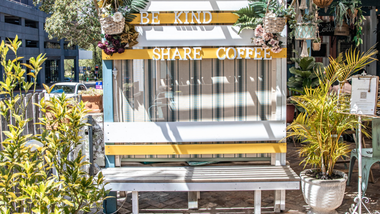 A pretty looking courtyard, with a sign that says: BE KIND, SHARE COFFEE